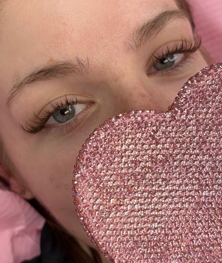 Close-up of client's eyes with eyelash extensions at Jiribeauty in Rockwall, Texas, US, holding a pink heart decor.