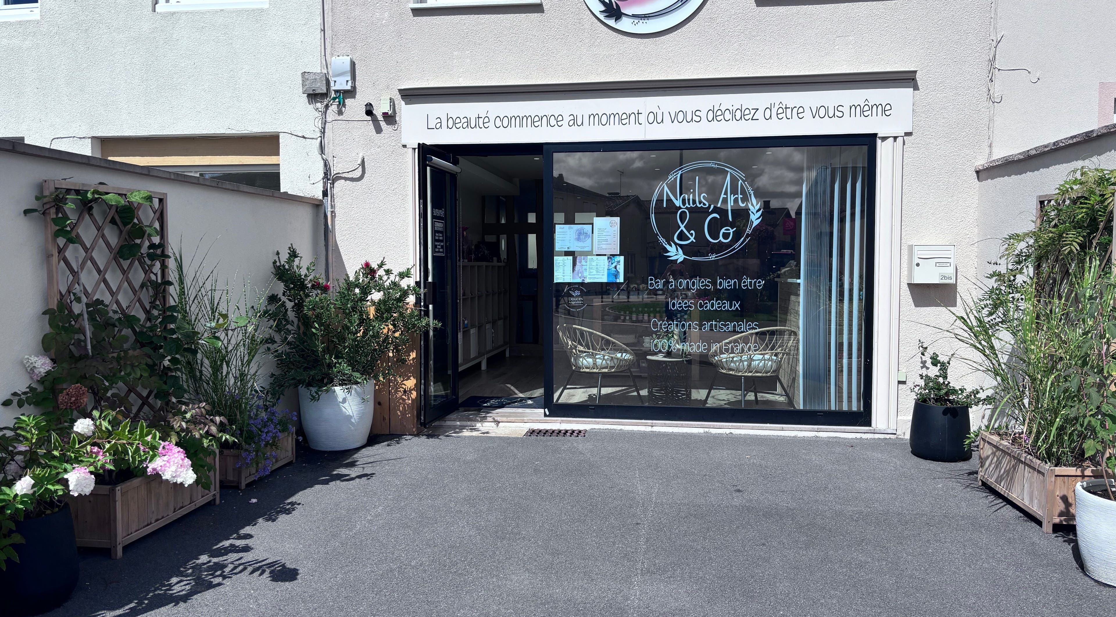 Entrée de Nails, Art & Co à Sarry, Grand Est, FR, entourée de plantes luxuriantes.