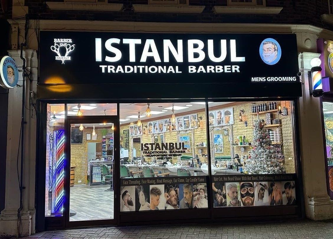 Exterior view of Istanbul Barber Rosehill in Sutton, England, GB, showcasing the illuminated shopfront at night.