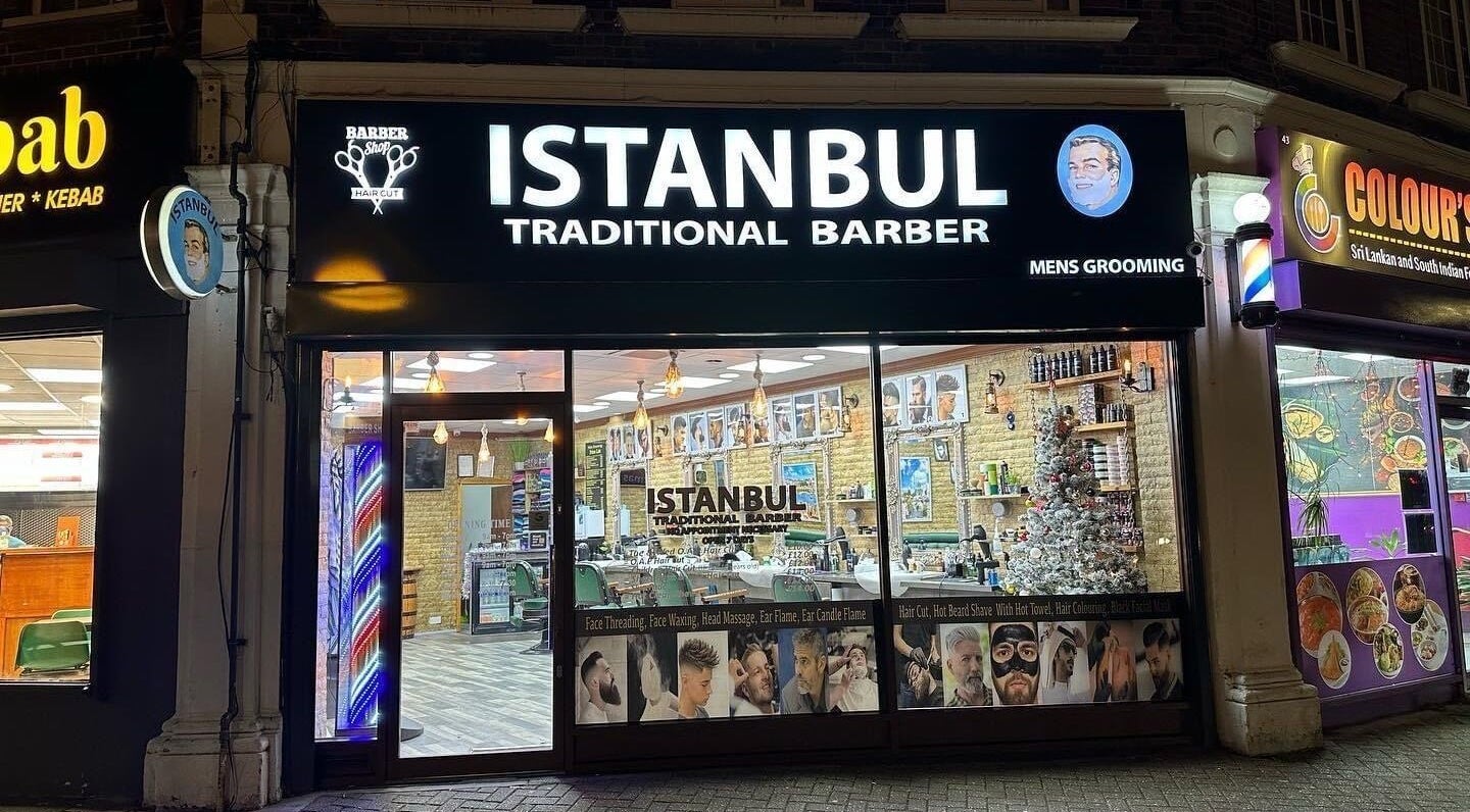 Exterior view of Istanbul Barber Rosehill in Sutton, England, GB, showcasing the illuminated shopfront at night.