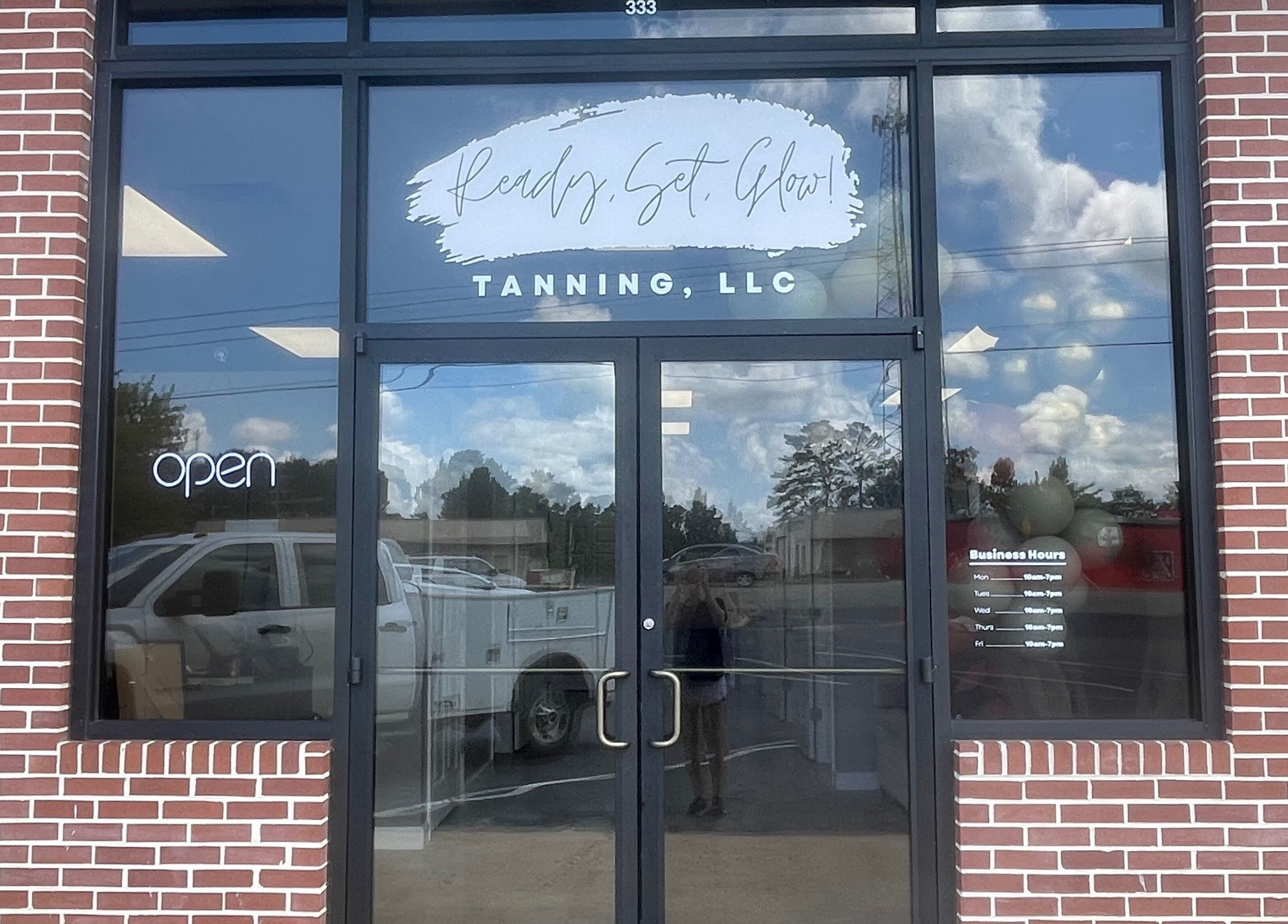 Front entrance of Ready Set Glow Tanning LLC, La Fayette, Alabama, US with glass doors and brick facade.