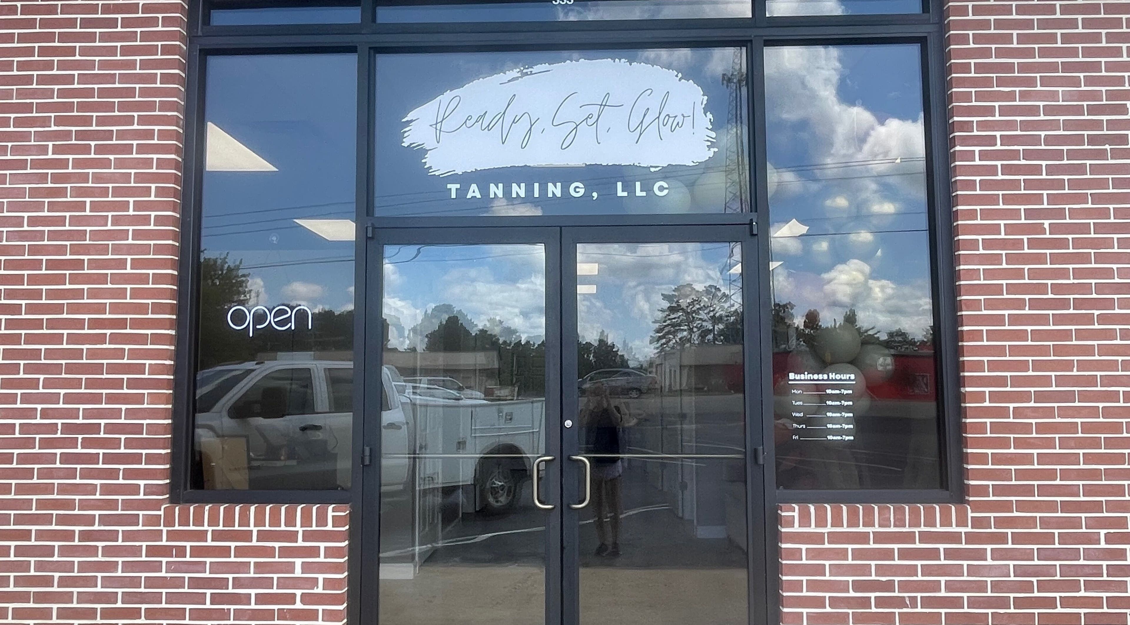 Front entrance of Ready Set Glow Tanning LLC, La Fayette, Alabama, US with glass doors and brick facade.