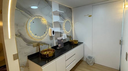 Baño moderno en Emy Study Nails, Bogotá, Bogotá, CO con espejo iluminado y lavamanos dorados.