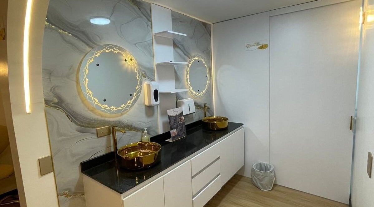 Baño moderno en Emy Study Nails, Bogotá, Bogotá, CO con espejo iluminado y lavamanos dorados.