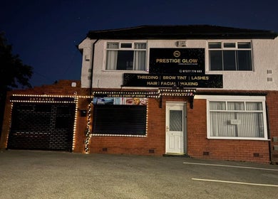 Exterior of Prestige Glow beauty salon in Bolton, England, GB, illuminated by decorative lights at night.