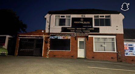 Exterior of Prestige Glow beauty salon in Bolton, England, GB, illuminated by decorative lights at night.