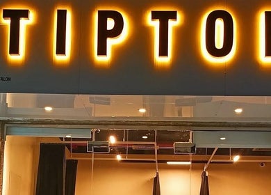 Entrance of Tiptoe Nailounge glowing with lights in Sharjah, AE, showcasing elegant exterior design.