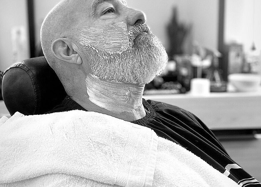 Hombre relajado en La casa del corte by Fifty, Tijuana, recibiendo afeitado profesional en barbero.