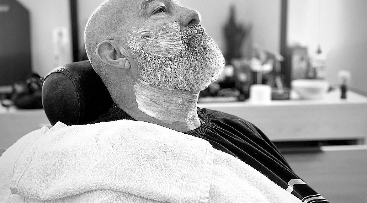 Hombre relajado en La casa del corte by Fifty, Tijuana, recibiendo afeitado profesional en barbero.