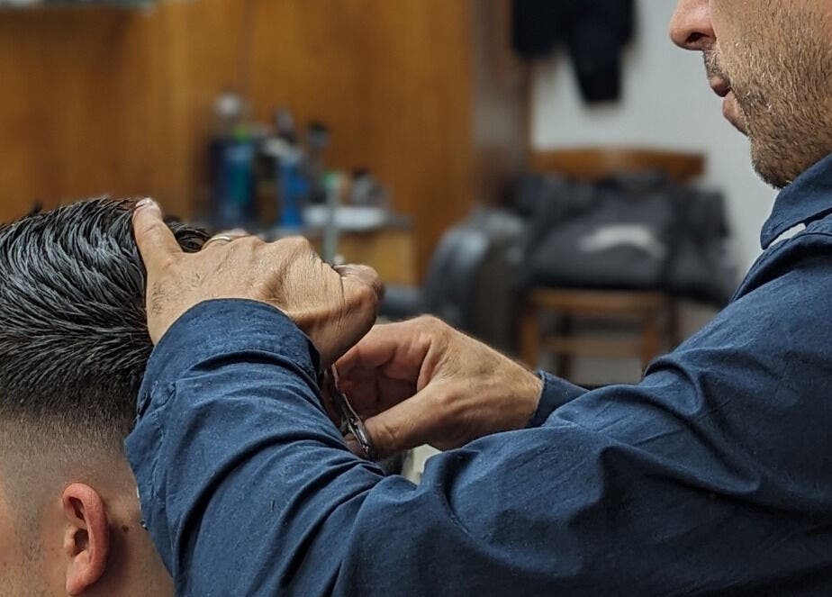 A barber at Wick Lane Barbershop in London, England, GB expertly styling a client's hair.