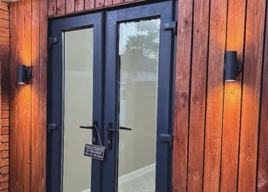 Elegant wooden entrance at Alora SkinSpecialist in Birmingham, England, GB, warmly lit for a tranquil welcome.