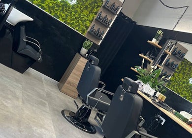 Interno moderno di Double G Barbershop a Selargius, Sardegna, IT con poltrone eleganti e decorazioni verdi.