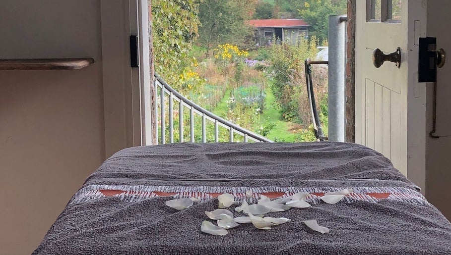 Tranquil massage table with rose petals at Serenity Massage, Grampound, England, GB, overlooking lush garden scenery.