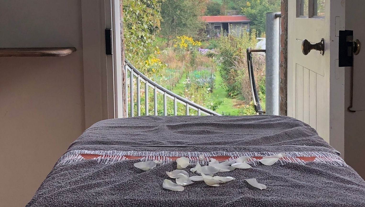 Tranquil massage table with rose petals at Serenity Massage, Grampound, England, GB, overlooking lush garden scenery.