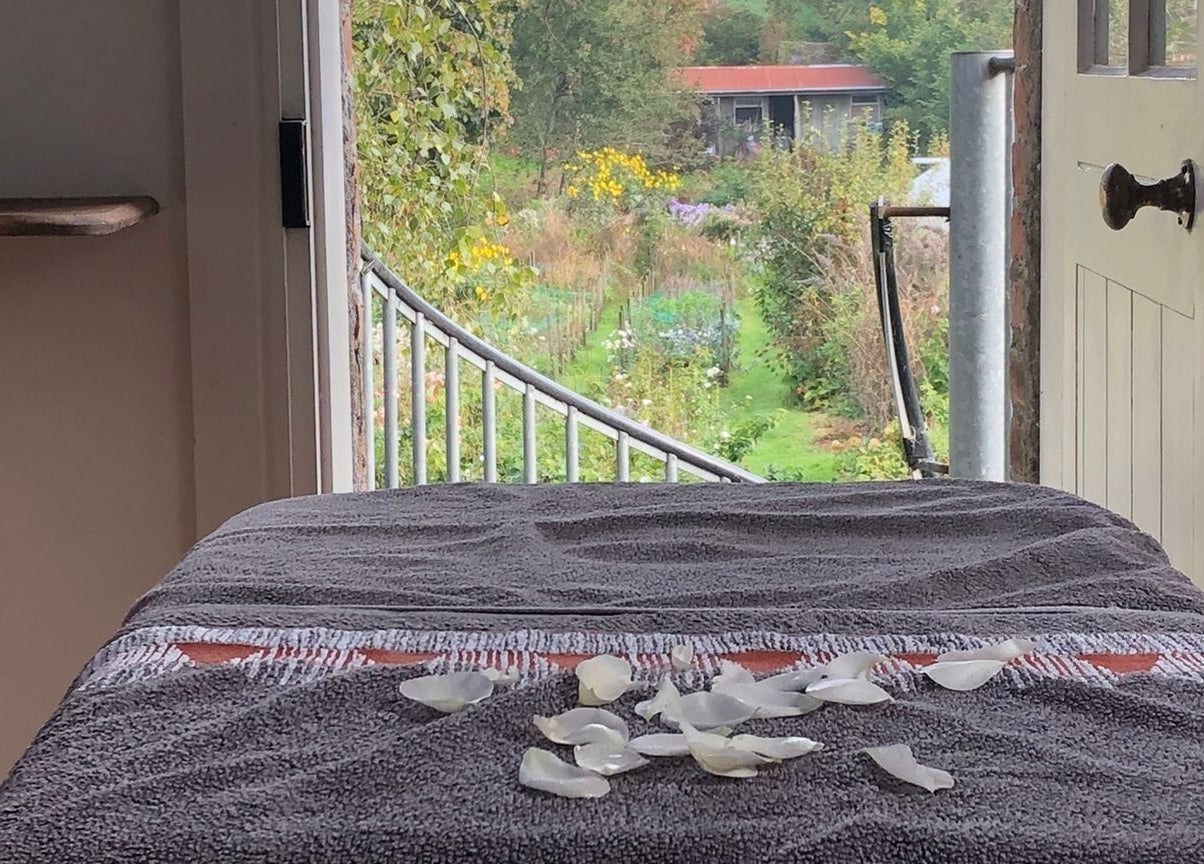 Tranquil massage table with rose petals at Serenity Massage, Grampound, England, GB, overlooking lush garden scenery.