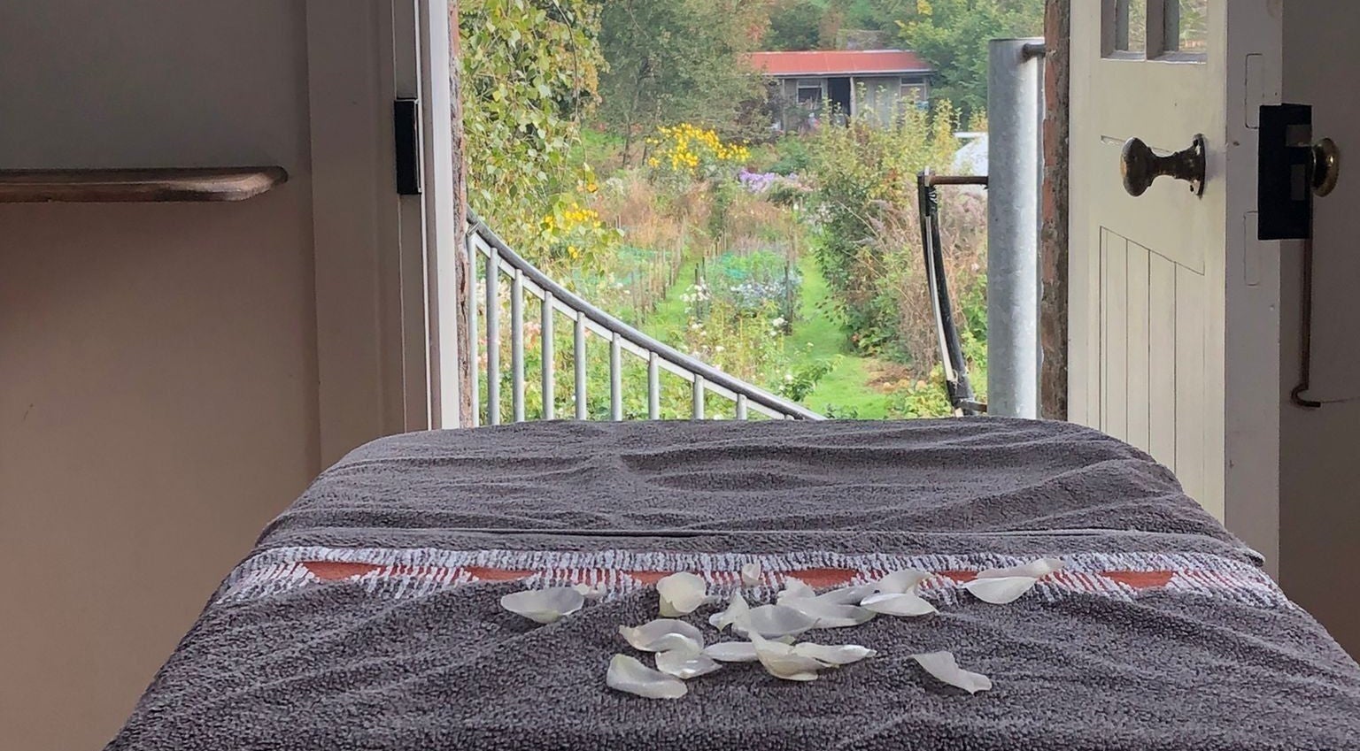 Tranquil massage table with rose petals at Serenity Massage, Grampound, England, GB, overlooking lush garden scenery.