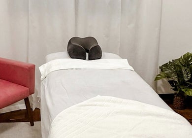 Sala de massagem no Lu Delivery Spa, São Paulo, com cama e poltrona rosa, ideal para relaxamento.