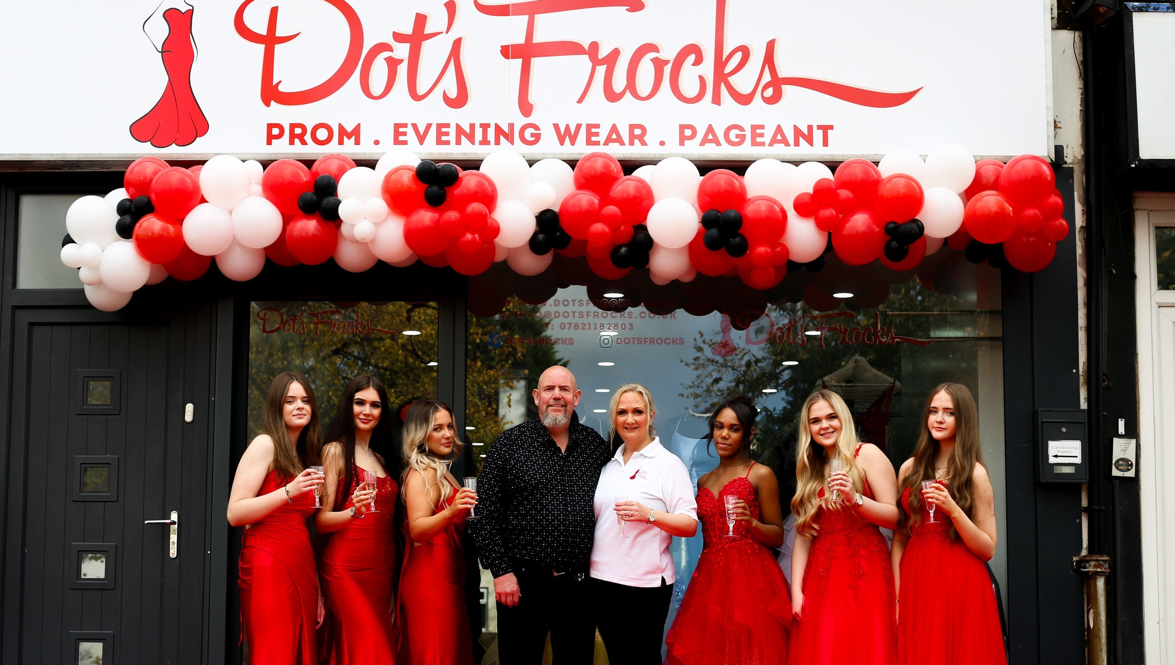 Group at Dot's Frocks entrance, Manchester, England, GB. Celebrating in red attire under balloon arch.