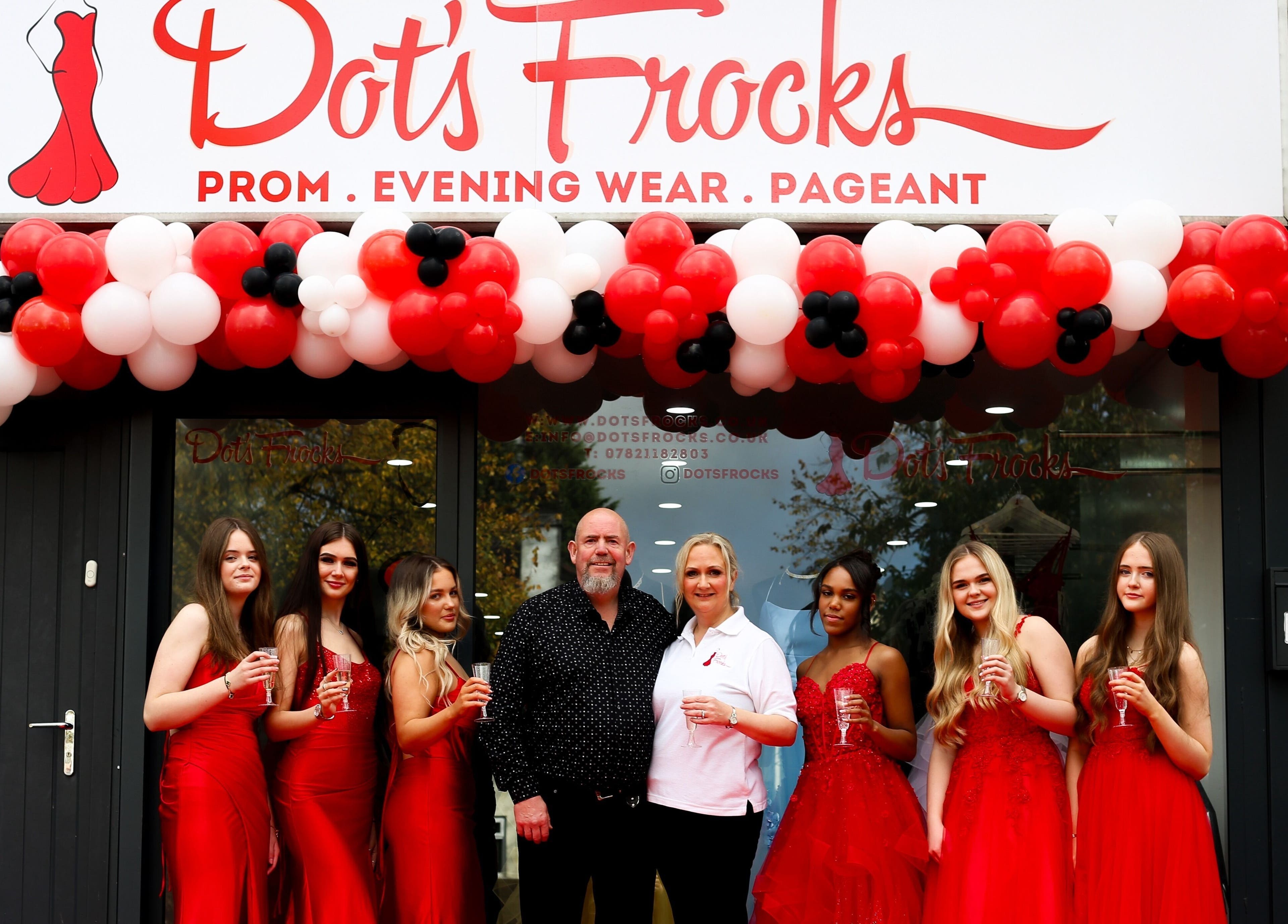 Group at Dot's Frocks entrance, Manchester, England, GB. Celebrating in red attire under balloon arch.