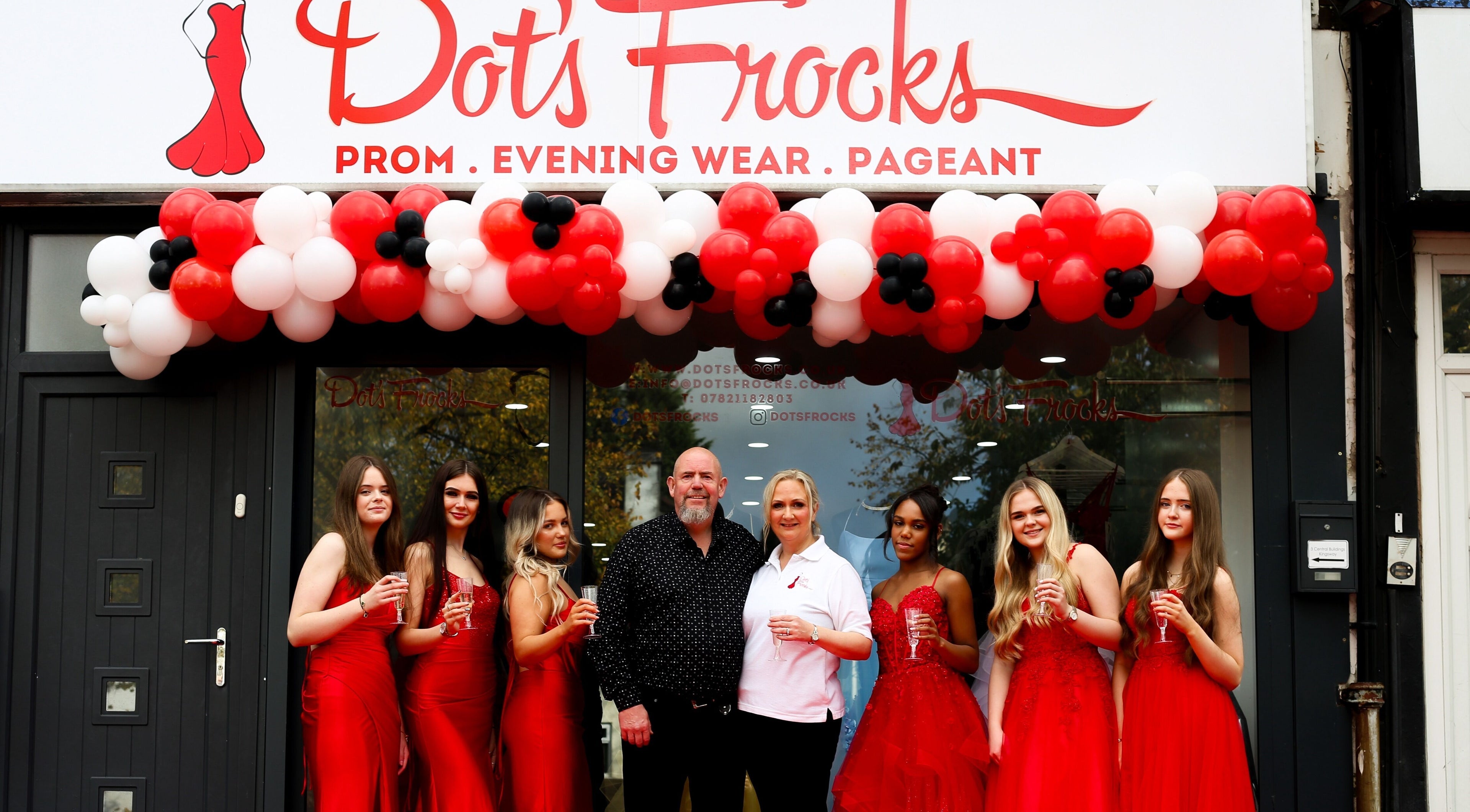 Group at Dot's Frocks entrance, Manchester, England, GB. Celebrating in red attire under balloon arch.