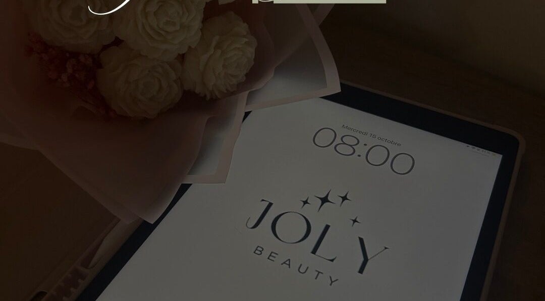 Tablette avec le logo JOLY BEAUTY à Meussia, Bourgogne-franche-comté, FR, à côté d'un bouquet de fleurs.