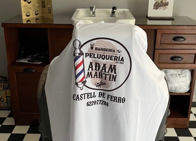 Interior de Barberia Adam Martin en Castell De Ferro, Andalucía, ES, mostrando una silla con logo distintivo.