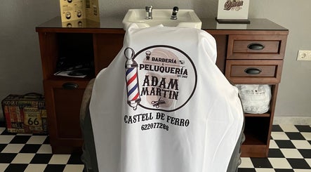 Interior de Barberia Adam Martin en Castell De Ferro, Andalucía, ES, mostrando una silla con logo distintivo.