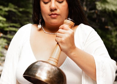A woman in white uses a sound bowl at LGHTTouch, Philadelphia, Pennsylvania, US, amidst a natural setting.