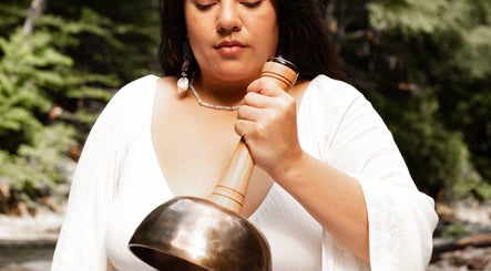 A woman in white uses a sound bowl at LGHTTouch, Philadelphia, Pennsylvania, US, amidst a natural setting.
