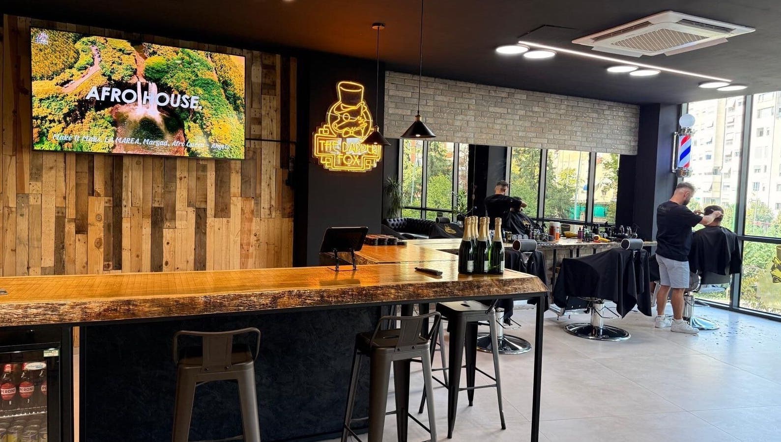 The Dapper Fox Barber in Tiranë, Tirana County, AL showcases a chic interior with a rustic bar and modern styling chairs.