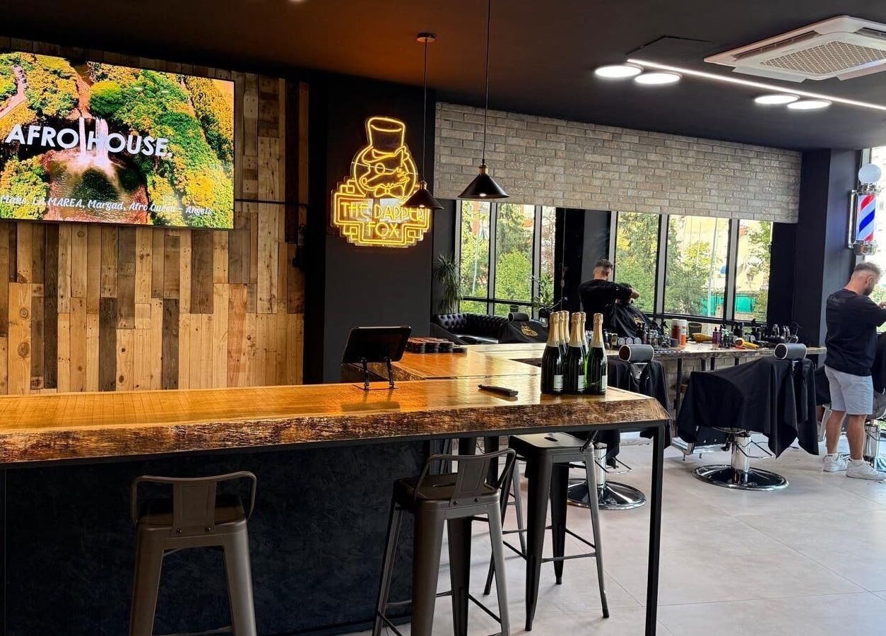 The Dapper Fox Barber in Tiranë, Tirana County, AL showcases a chic interior with a rustic bar and modern styling chairs.