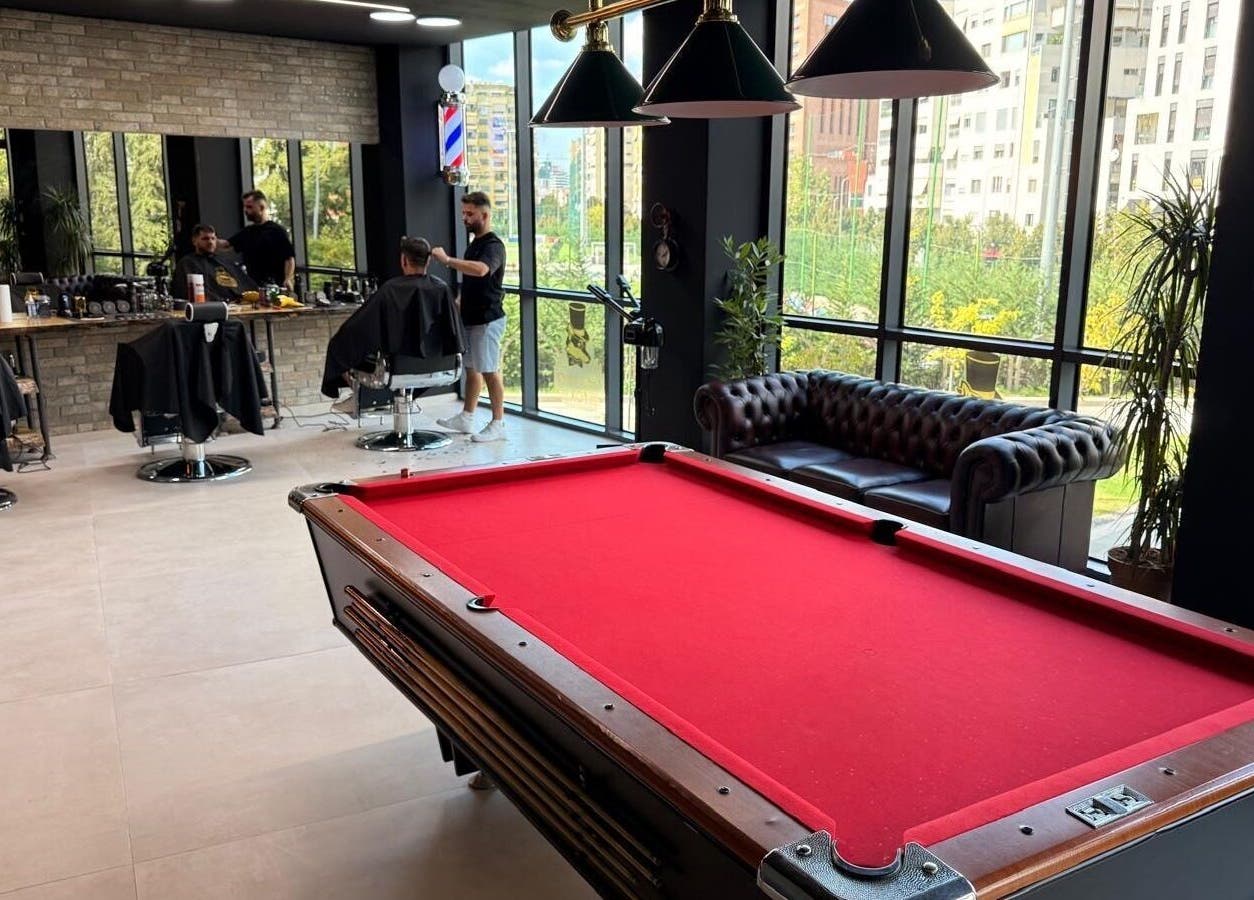 Modern interior of The Dapper Fox Barber in Tiranë, Tirana County, AL with a red pool table and stylish seating.