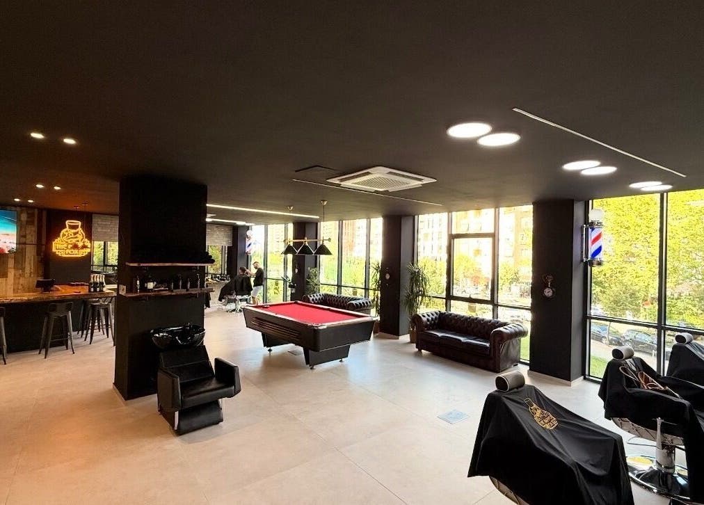 Modern interior of The Dapper Fox Barber in Tiranë, featuring sleek chairs and pool table.