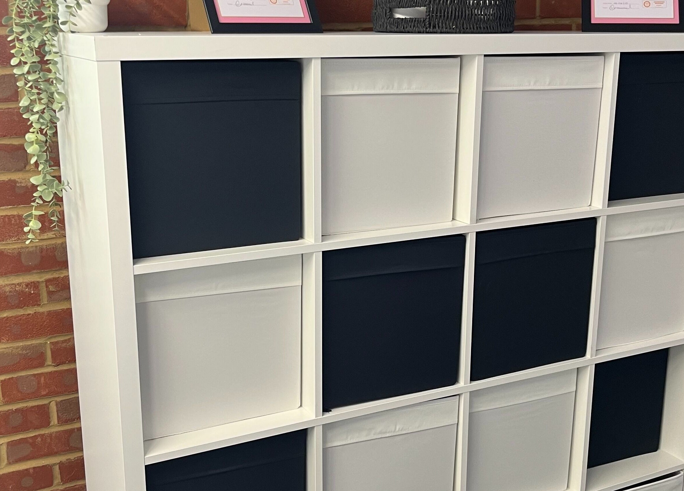Modern storage shelf at AW House Of Aesthetics, Wick, England, displaying certificates and greenery.