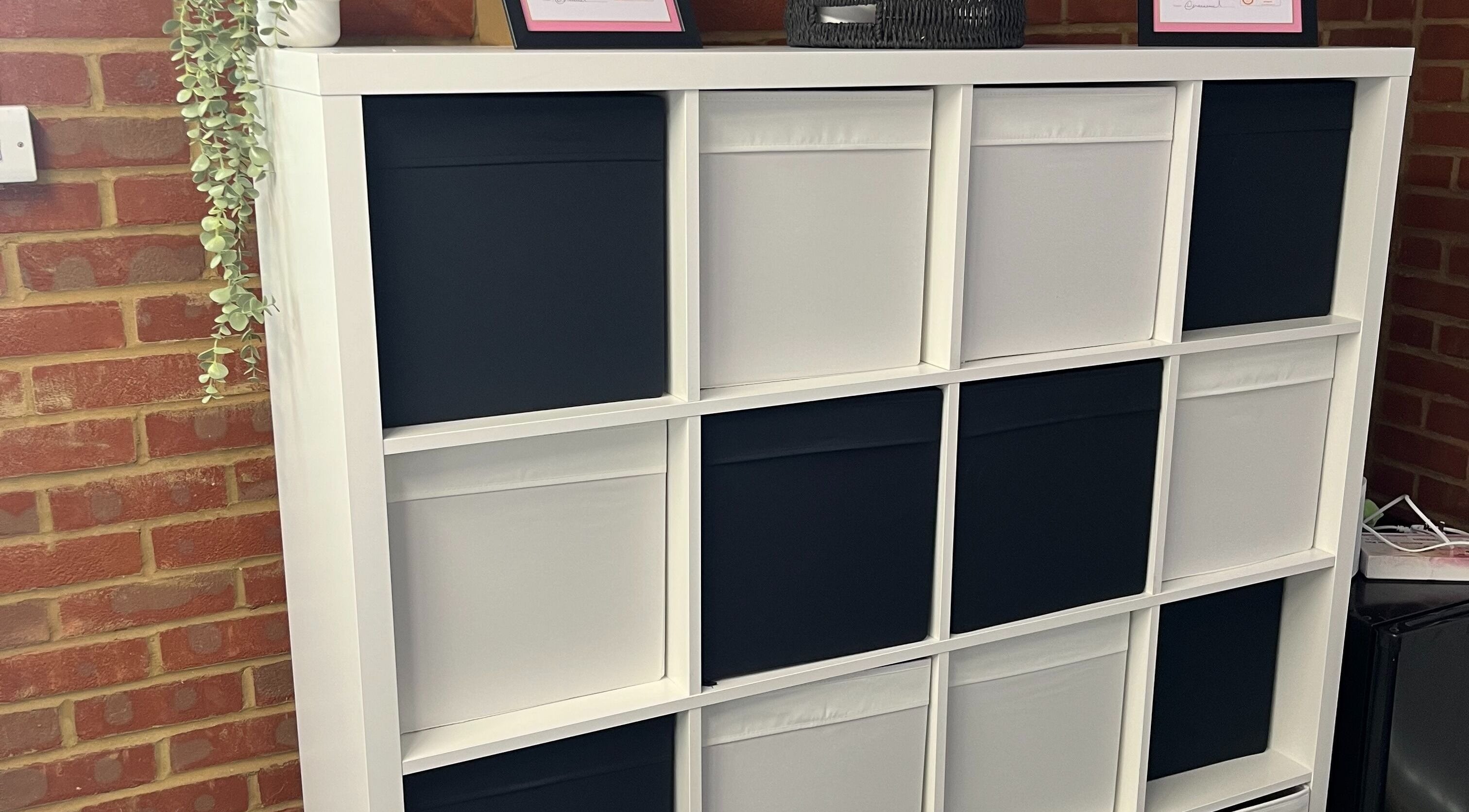 Modern storage shelf at AW House Of Aesthetics, Wick, England, displaying certificates and greenery.