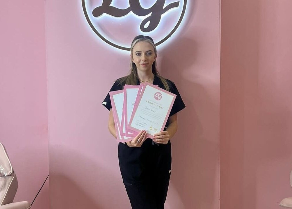 Woman holding certificates at AW House Of Aesthetics in Wick, England, GB with a pink backdrop and logo.