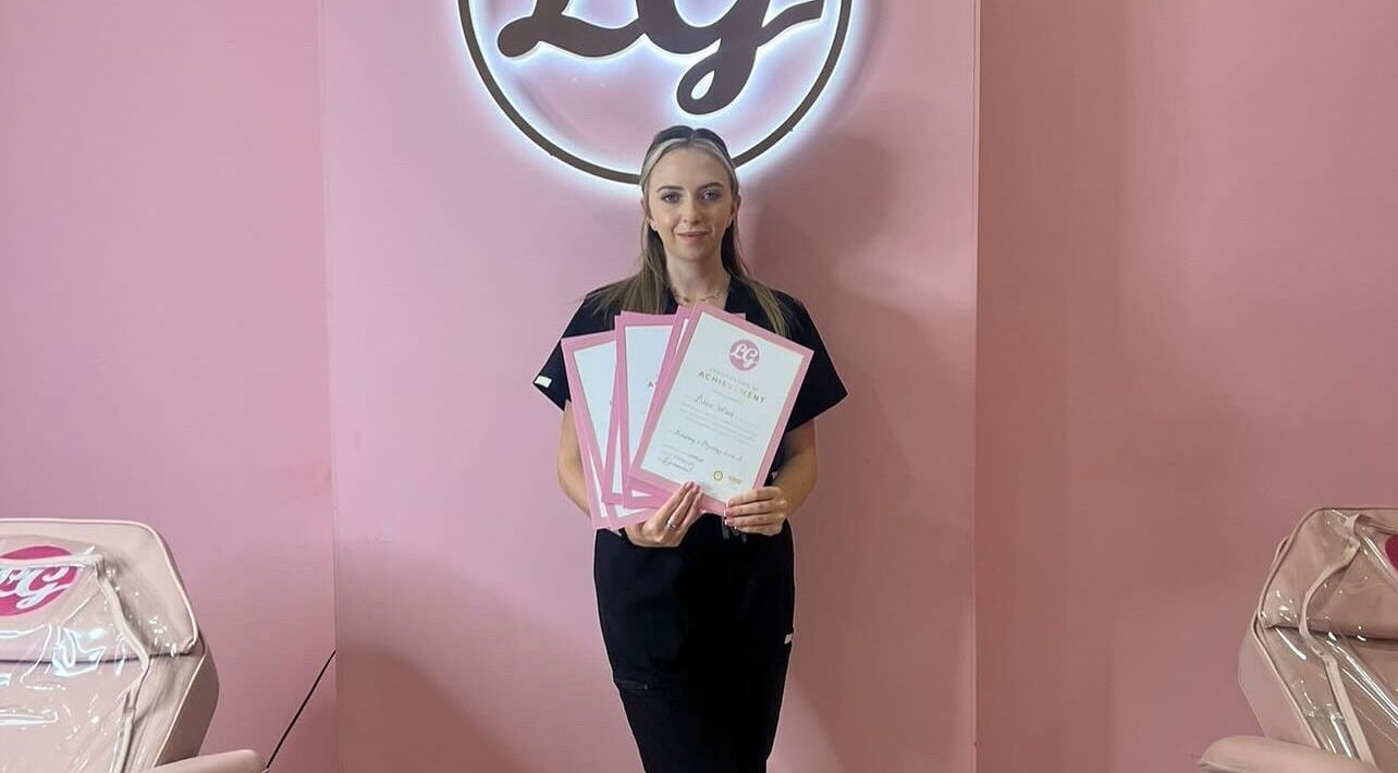 Woman holding certificates at AW House Of Aesthetics in Wick, England, GB with a pink backdrop and logo.