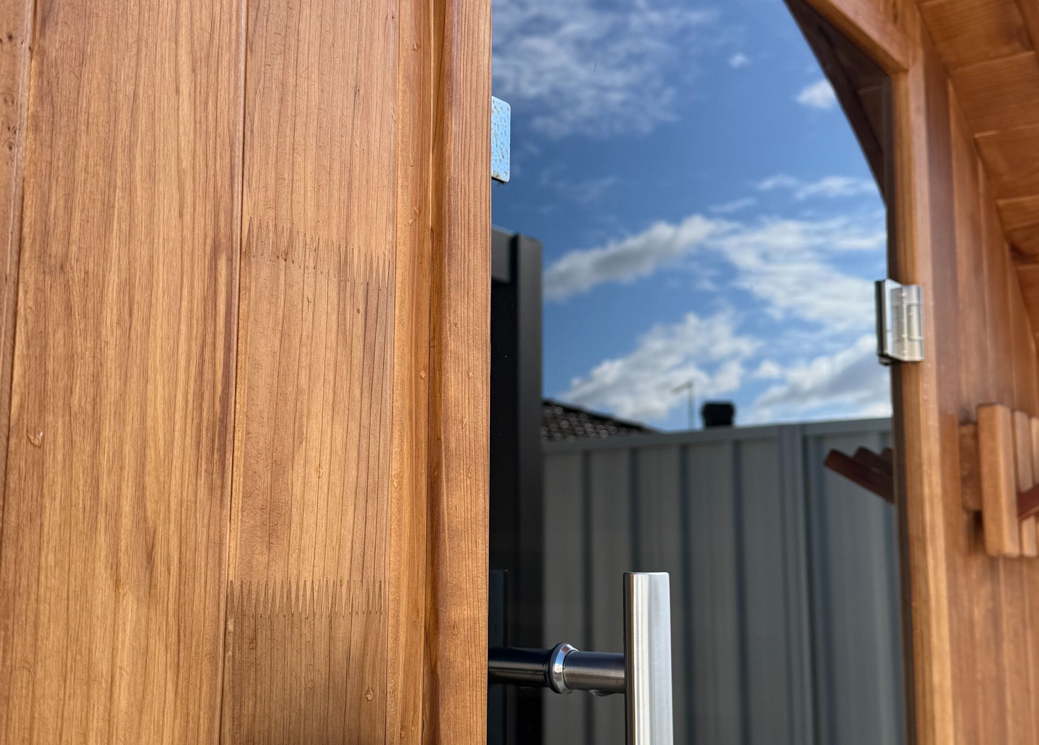 Wooden sauna door with handle at Rise and Fall Wellness, Kallaroo, Western Australia, AU under blue sky.