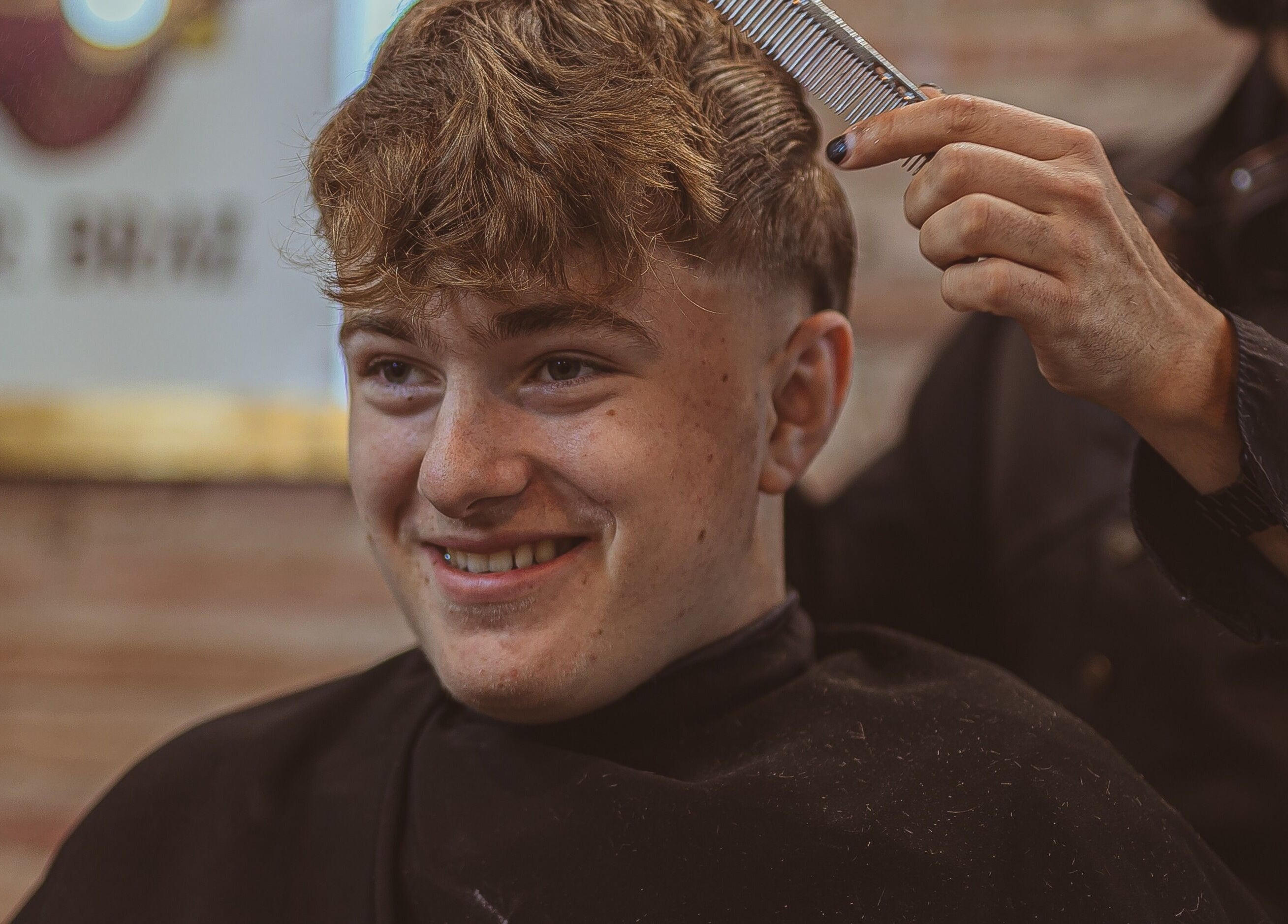 Joven sonríe mientras recibe corte de pelo en Mr. Braz Steampunk Barbershop, Barcelona, Catalunya, ES.