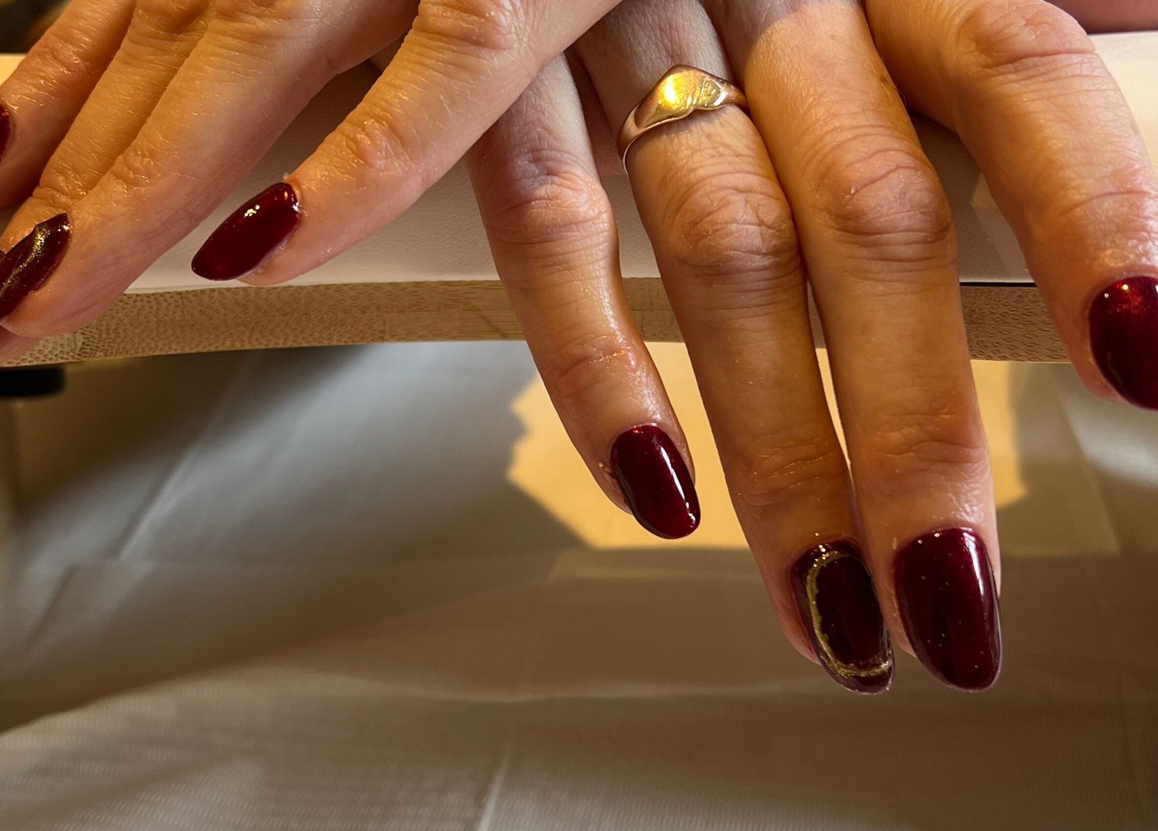 Crimson manicured nails at The Nail Studio By Kim, Leek, England, GB on a wooden rest.