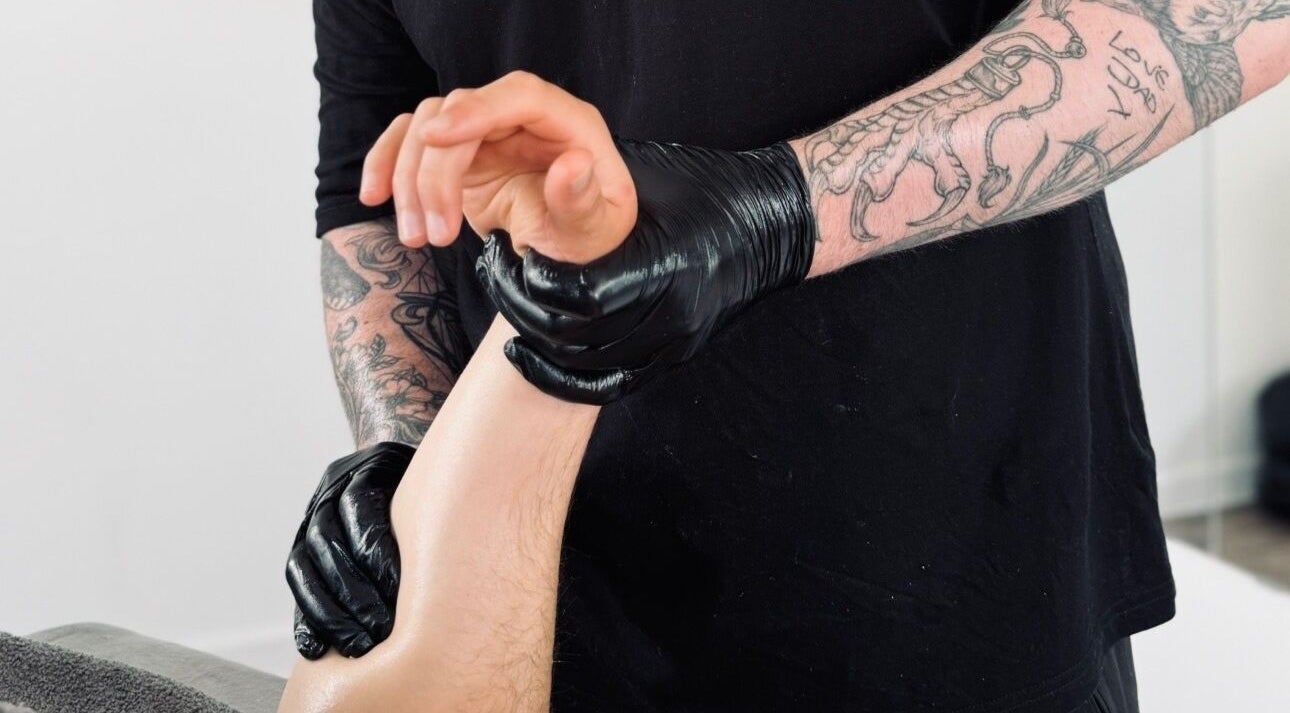 Therapist at Dan Orchard Sports Massage, Exeter, England, GB performing a forearm massage in black gloves.