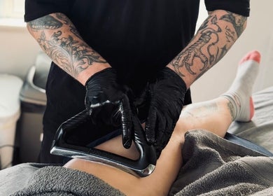 Tattooed therapist using massage tool at Dan Orchard Sports Massage, Exeter, England, GB.