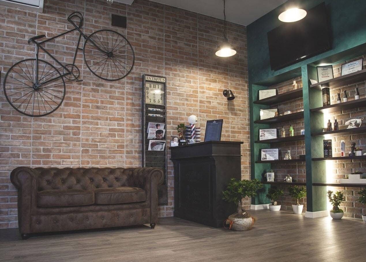 Interno di From Zero Barberia Lucana in stile industriale a Matera, Basilicata, IT con divano in pelle e scaffali.