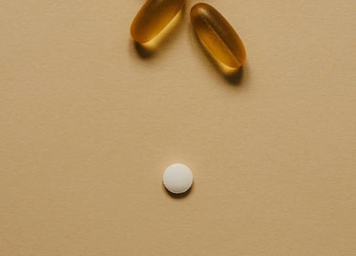 Two softgel capsules and a tablet on a beige background at Pharmable, London, GB.