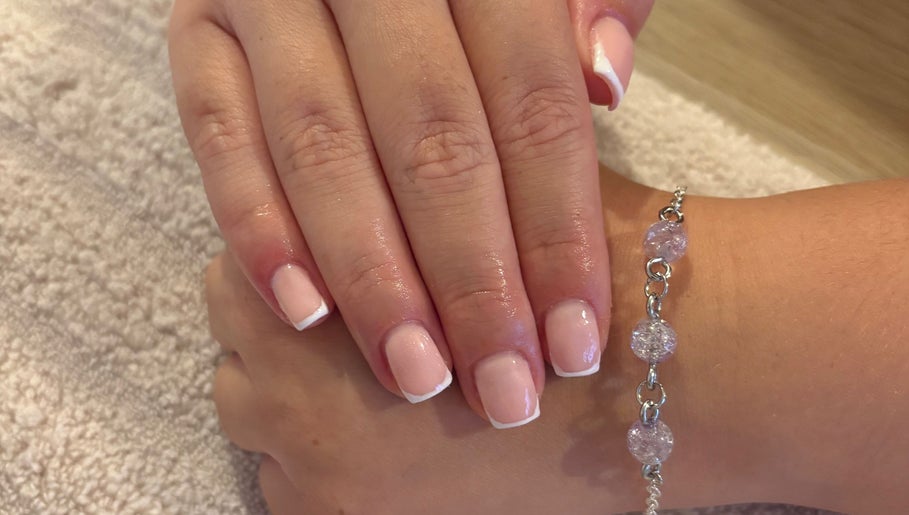 Elegant French manicure at EviemaiNails in Witham, England, GB showcasing glossy finish and a charm bracelet.