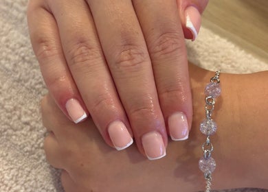 Elegant French manicure at EviemaiNails in Witham, England, GB showcasing glossy finish and a charm bracelet.