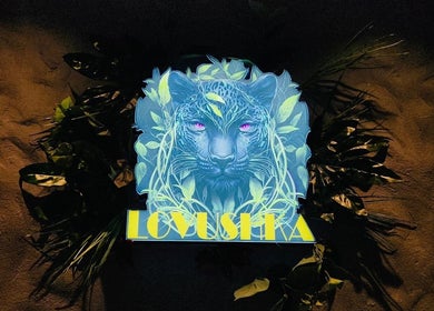 Illuminated leopard sign at Lovushka Beauty Salon in Doha, Doha Municipality, QA, surrounded by lush leaves.