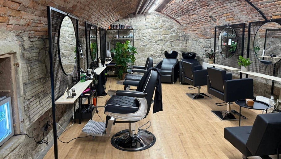 Interno elegante di Sa-Rc Italia Coiffeur Bern, in Bern, Bern, CH, con sedie nere e muri in pietra.