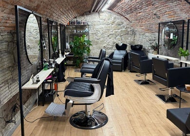 Interno elegante di Sa-Rc Italia Coiffeur Bern, in Bern, Bern, CH, con sedie nere e muri in pietra.
