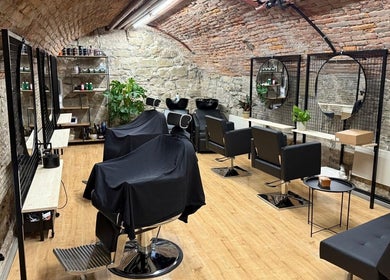 Interno rustico ed elegante di Sa-Rc Italia Coiffeur Bern a Bern, Bern, CH con poltrone nere e specchi circolari.